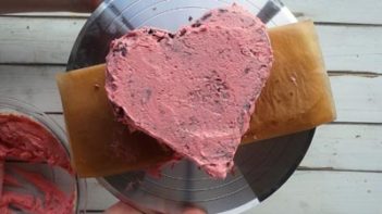 heart shaped cake on a cake stand with a thin coat of frosting