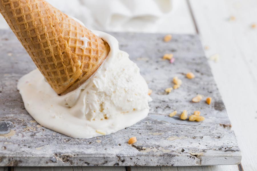 an ice cream cone upside down and melting on a marble slab with nuts around