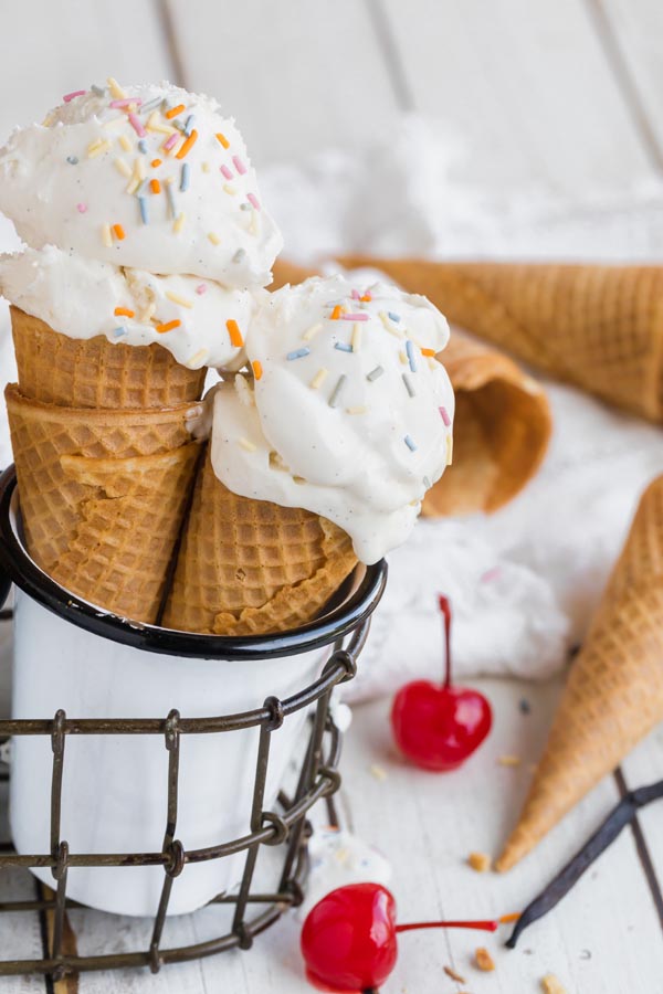 two ice cream cones in a cup with two red cherries near by