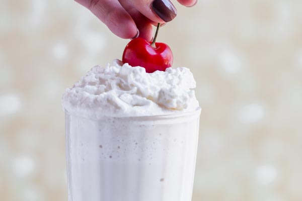 placing a cherry on top of a vanilla milkshake