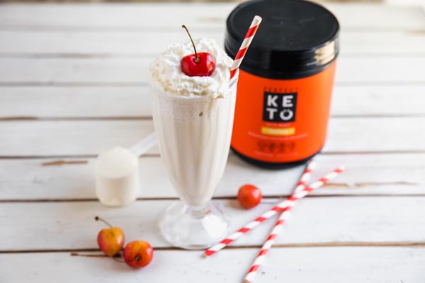 keto vanilla milkshake with protein powder in the background and a couple of red and white straws