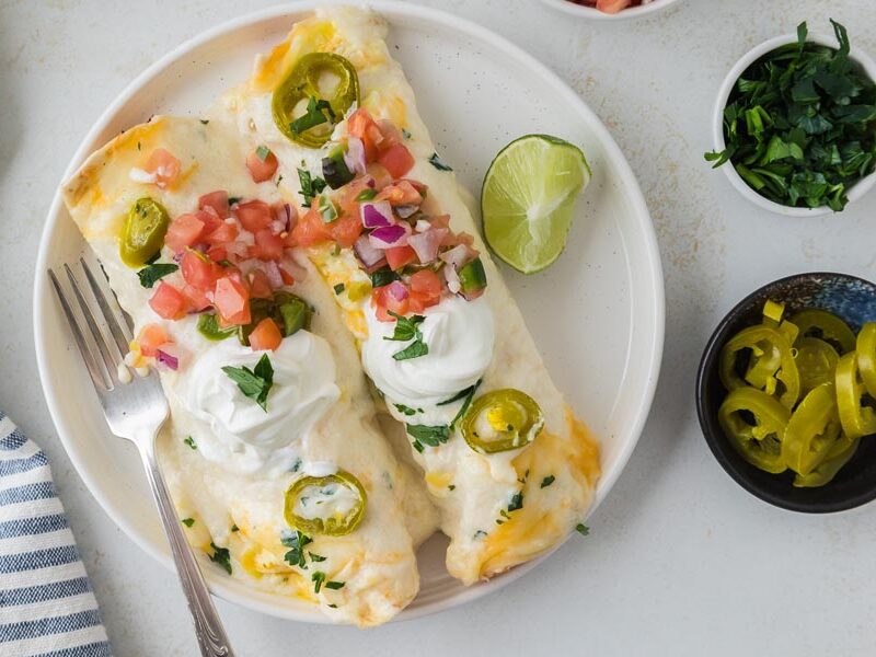 Two chicken enchiladas with white sauce, pico de gallo, sour cream and jalapenos.