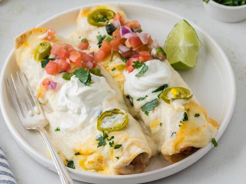 Two creamy white chicken enchiladas on a plate with a fork topped with pico de gallo.