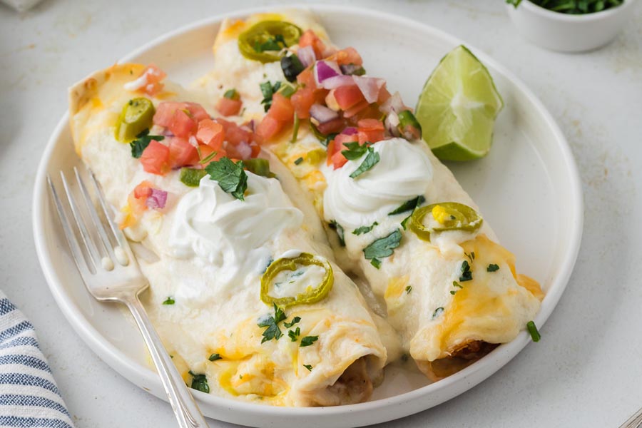 Two creamy white chicken enchiladas on a plate with a fork topped with pico de gallo.