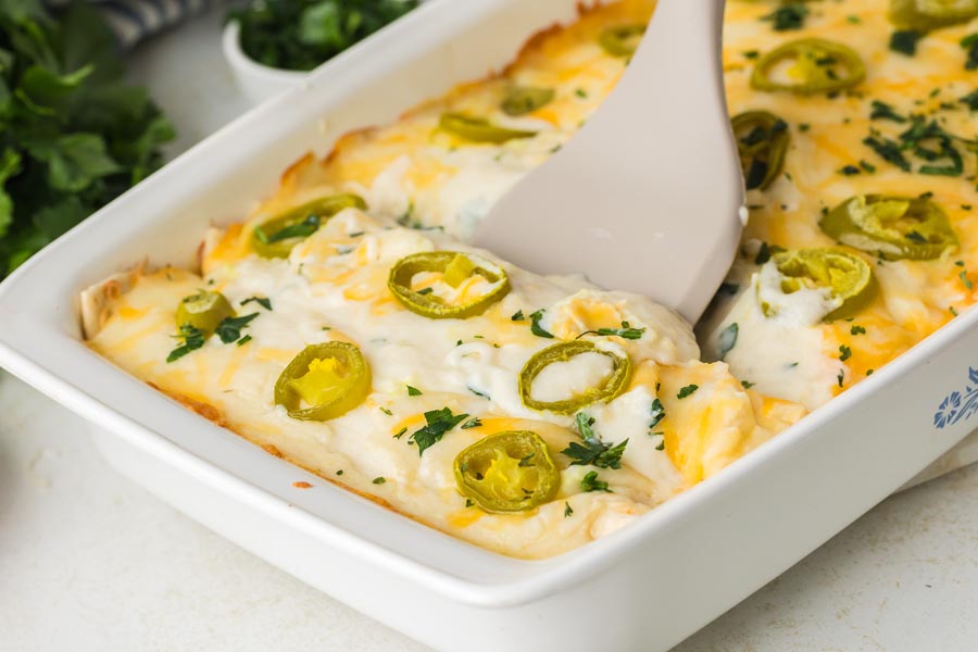 A spatula scooping out a serving of white chicken enchiladas in a creamy sauce.