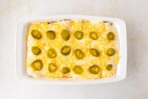 White chicken enchiladas topped with shredded cheese and pickle jalapenos ready to go into the oven.