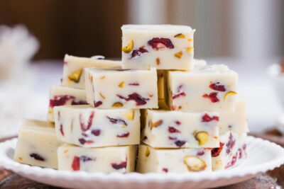 White chocolate fudge with cranberries and pistachios stacked on a white plate.