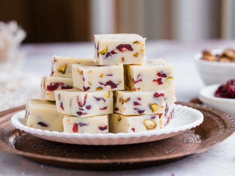 Stacked white chocolate fudge with cranberries and pistachios on a white plate.