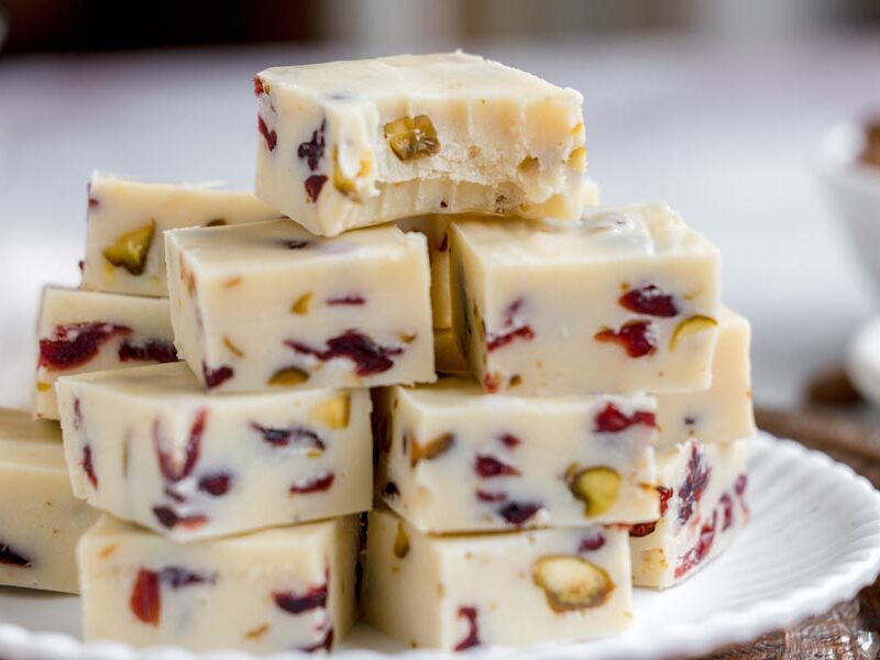 A bite is taken out of the top piece of a tall stack of white chocolate cranberry pistachio fudge.