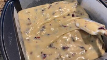 The warm cranberry pistachio fudge mixture is spread evenly into a parchment-lined baking pan.