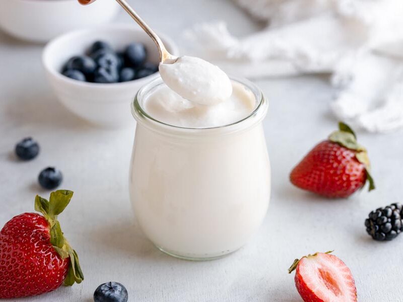 A spoon scooping up a spoonful of yogurt with berries nearby.
