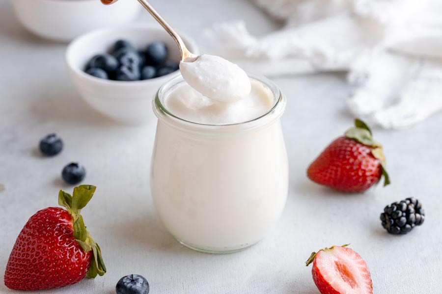 A spoon scooping up a spoonful of yogurt with berries nearby.