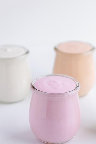 Three jars of yogurt. One is pink and the two in the back are white and orange.