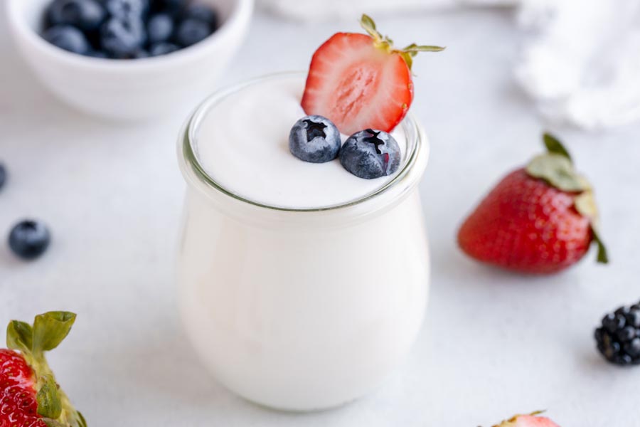 A small jar of homemade yogurt topped with berries and a bowl of blueberries to the rear.