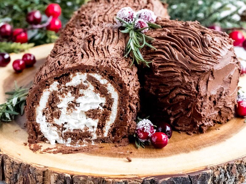 Chocolate Yule log cake with chocolate frosting, cream swirl, sugared cranberries and rosemary.