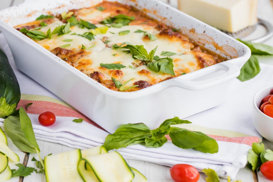 a white casserole dish with lasagna and green herbs scattered around