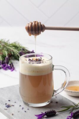 Honey being drizzled over a frothy mug of lavender milk tea garnished with dried lavender.