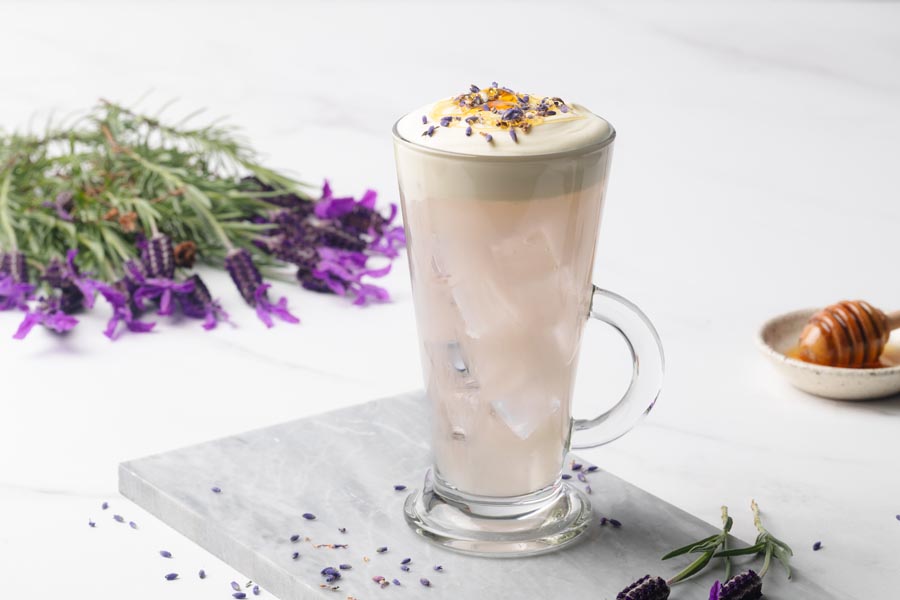 Iced lavender milk tea served in a tall glass with ice, creamy foam, and dried lavender buds on top.