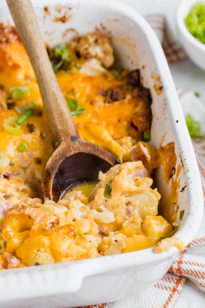 a white casserole dish with cauliflower, cheese, bacon and green onion