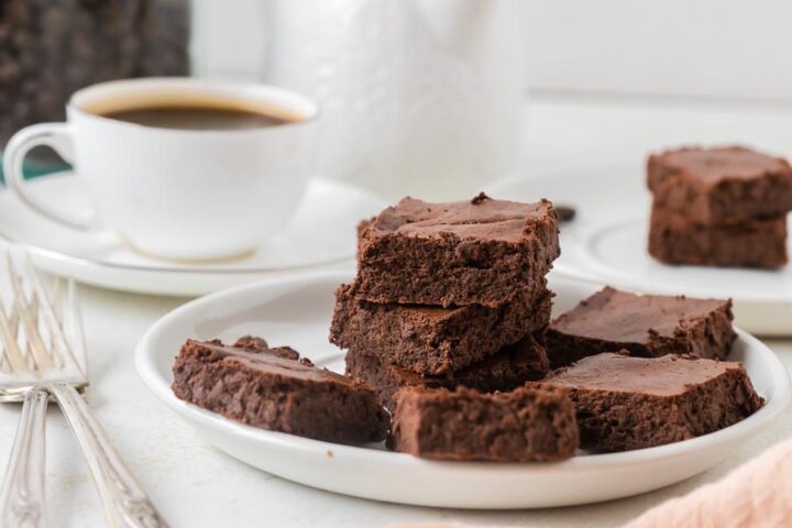 A plate stacked with fudgy low-calorie brownies is served alongside a cup of black coffee.