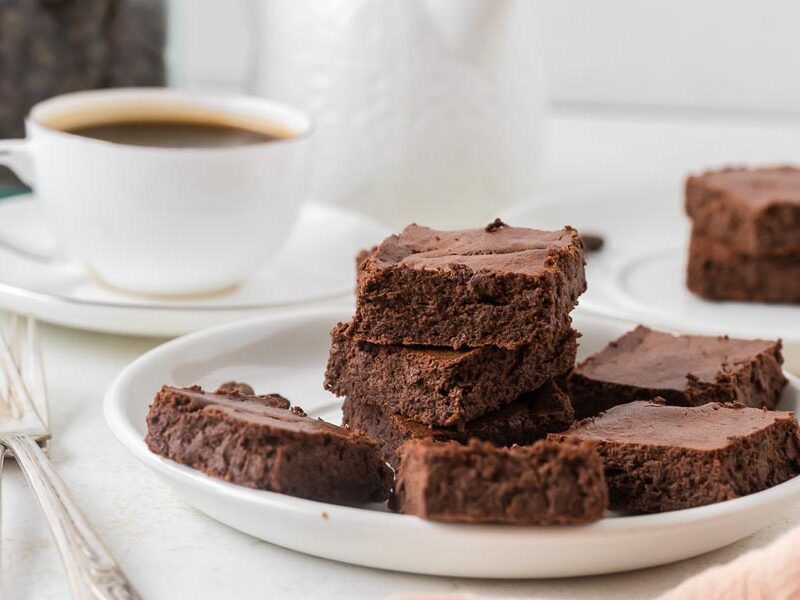 A plate stacked with fudgy low-calorie brownies is served alongside a cup of black coffee.