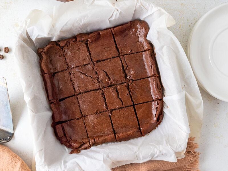 Overhead view of freshly baked brownies cut into squares inside a parchment-lined baking dish.