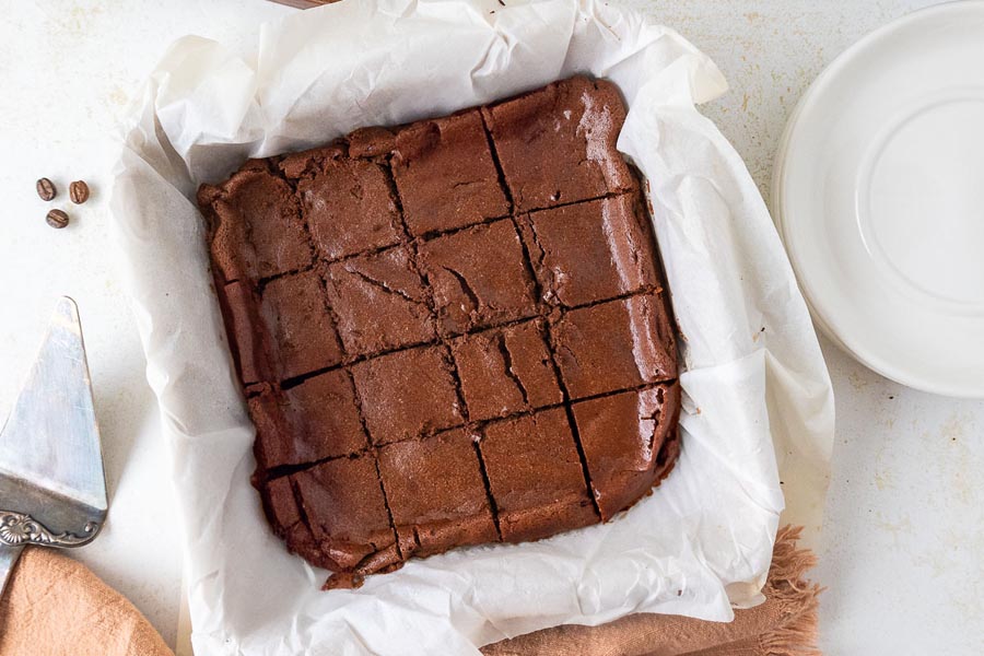 Overhead view of freshly baked brownies cut into squares inside a parchment-lined baking dish.