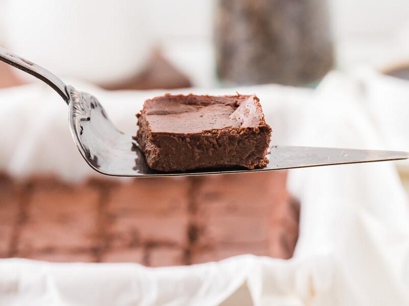A close-up of a single fudgy brownie on a metal spatula, showing its soft, dense texture.