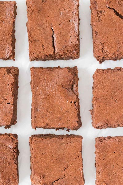 Neatly arranged rows of crackly-topped brownies on a sheet of white parchment paper.