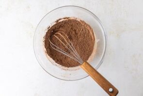 A glass bowl filled with cocoa powder mixture being whisked with a wooden-handled whisk.