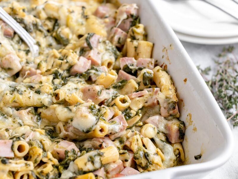 Ham and Swiss ziti casserole with creamy cheese sauce and spinach in a white baking dish.