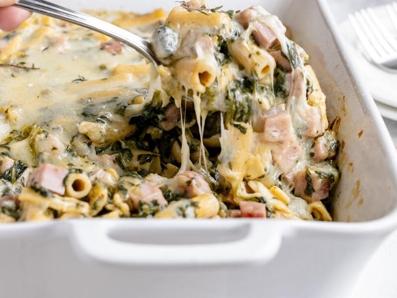 Spoon lifting a cheesy portion of ham and Swiss ziti casserole showing melted cheese and tender pasta.