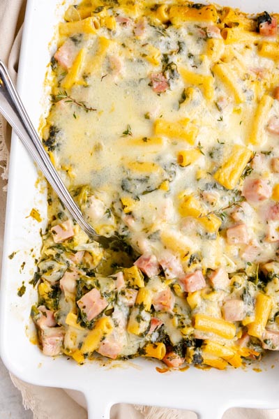 Close-up of cheesy ham and Swiss ziti casserole highlighting melted cheese, spinach, and chunks of ham.