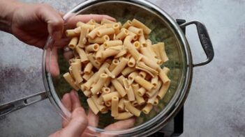 Cooked lupini ziti pasta being drained in a colander over a pot.