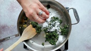 Chopped spinach being cooked in a skillet with seasoning and thickener added.