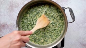Creamy spinach sauce being stirred in a skillet until smooth and thickened.