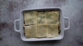 Pasta mixture spread into a baking dish and topped with slices of Swiss cheese before baking.