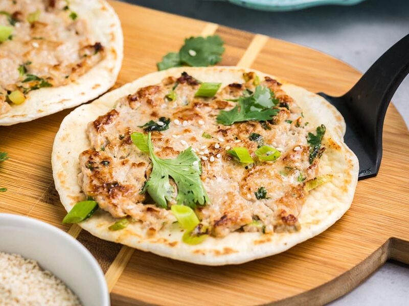 Grilled smashed taco filling with ground chicken and Asian spices on a wooden cutting board.