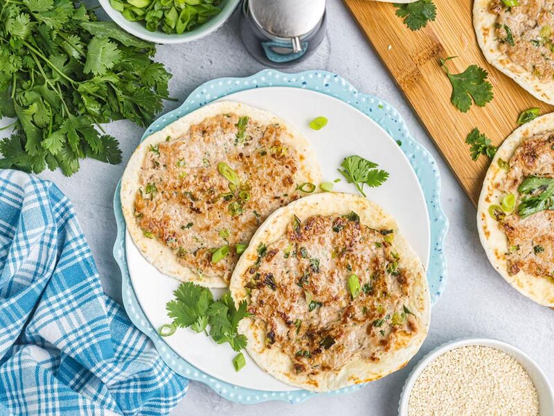 Two smashed dumpling tacos on a blue plate topped with green onion, cilantro and sesame seeds.