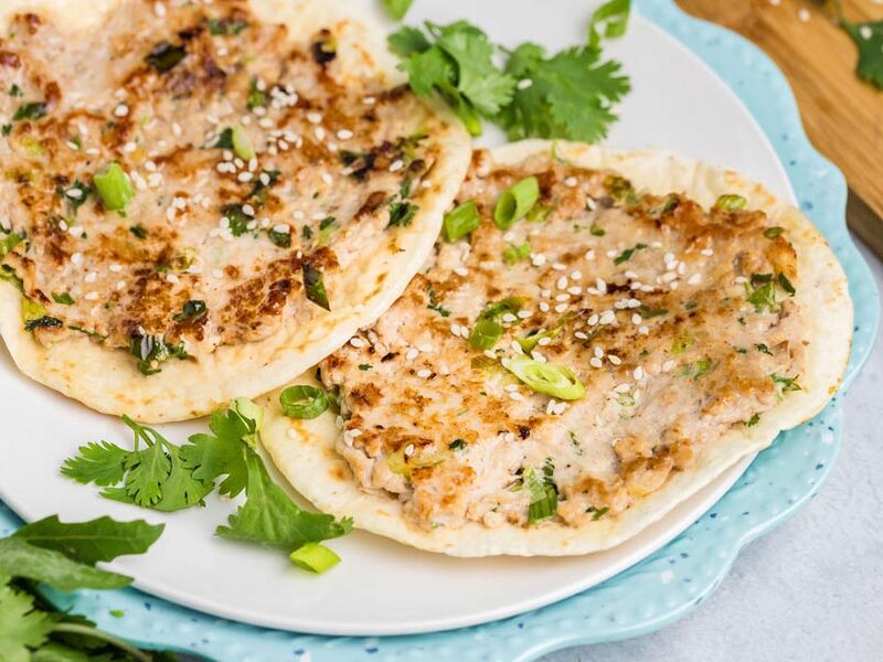 Fried smashed chicken tacos on a plate topped with cilantro, sesame seeds and green onion.