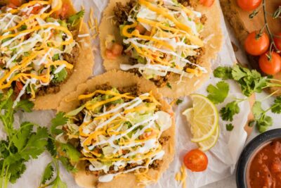 three beef tostadas on parchment paper with limes, cilantro and tomatoes around