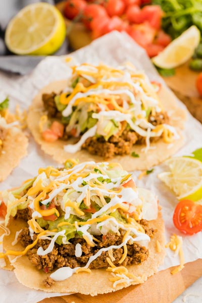 two beef tostadas on a board with cheese and pico and sour cream