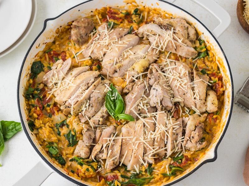 Looking down into a skillet filled with sliced chicken on top of a creamy orzo Italian pasta dish.