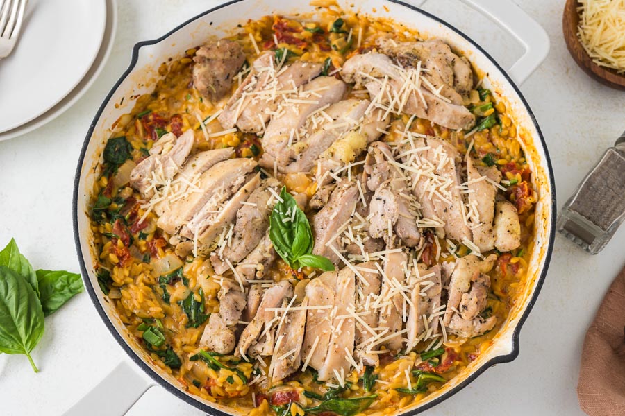 Looking down into a skillet filled with sliced chicken on top of a creamy orzo Italian pasta dish.