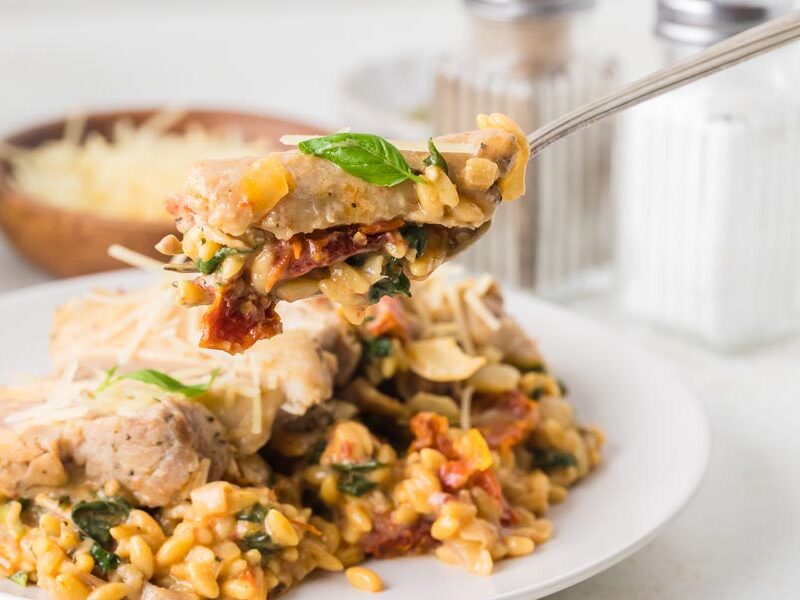 A fork holding a bite of Italian tuscan chicken pasta.