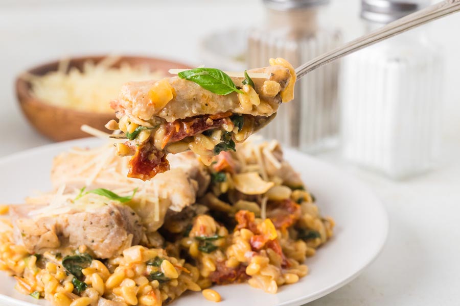 A fork holding a bite of Italian tuscan chicken pasta.