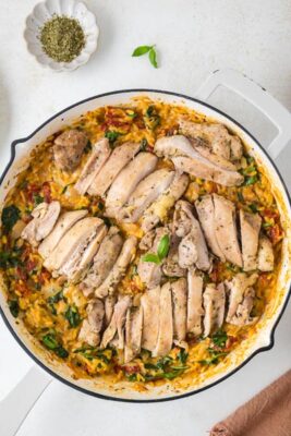 A white cast iron skillet filled with a creamy orzo pasta and cooked slice chicken thighs.
