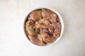 A bowl with marinaded skinless, boneless chicken thighs.
