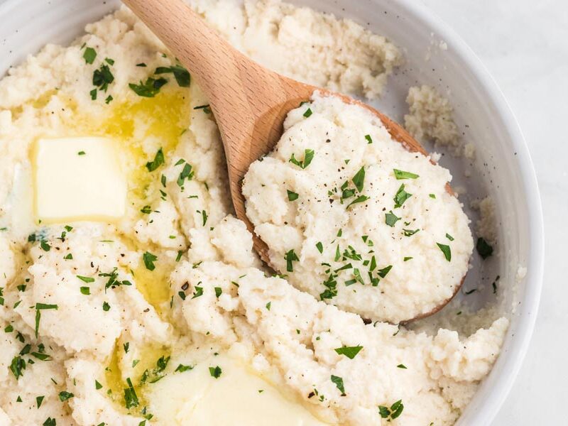 Mashed turnips with melting butter, parsley and a wooden serving spoon.
