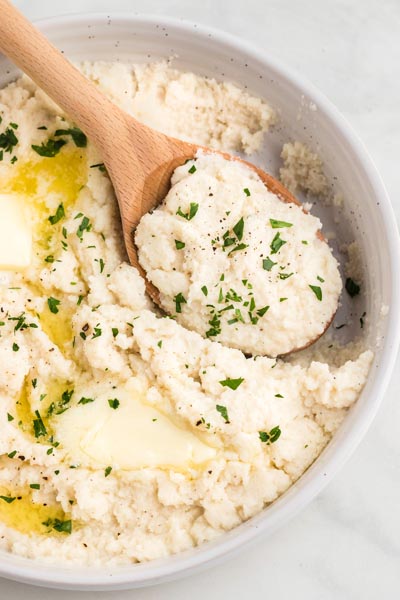 A wood spoon inside a dish filled with mashed turnips.